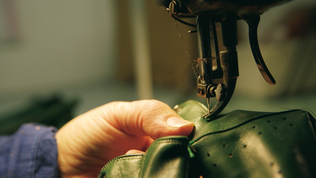 Cucitura artigianale di un guanto in pelle verde