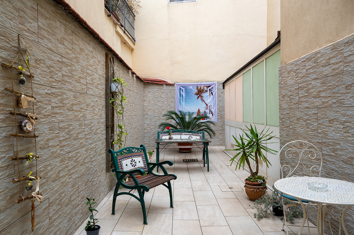 Der Innenhof von Gloves Rooms mit Bank aus Eisen und Mosaik, Pflanzen und kleinem Tisch